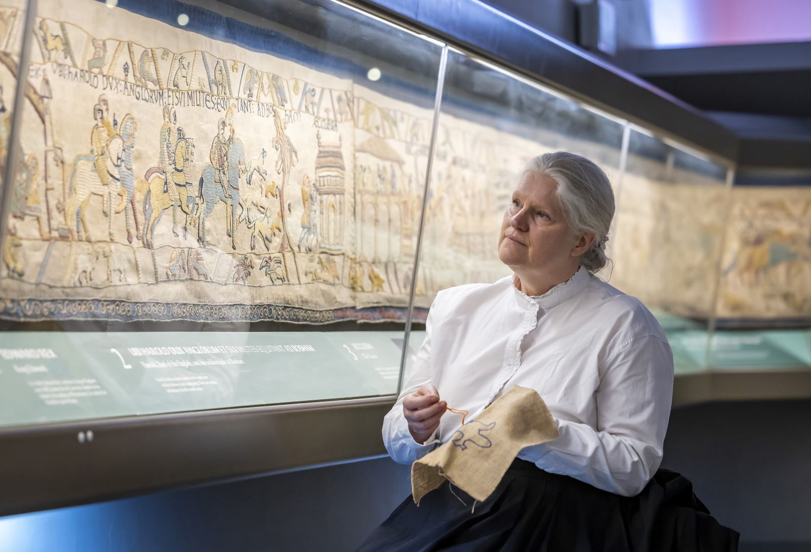 Lady in victorian costume embroidering beside Britain's Bayeux Tapestry